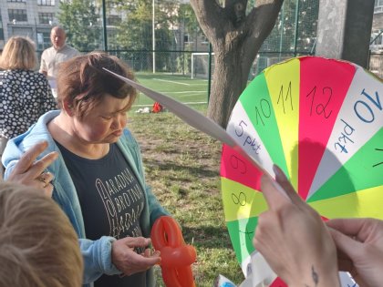 Na zdjęciu widać kobietę w srednim wieku oglądającą kolorowe gadżety,przed kobietą widnieje kolorowa tarcza do gry w tle zielony ogród