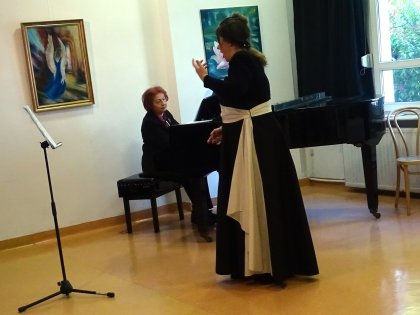 Śpiewaczka w czarnej sukni występuje obok pianistki przy fortepianie