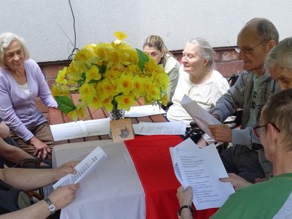 Seniorzy wokół ozdobionego Flagą Polski Stołu