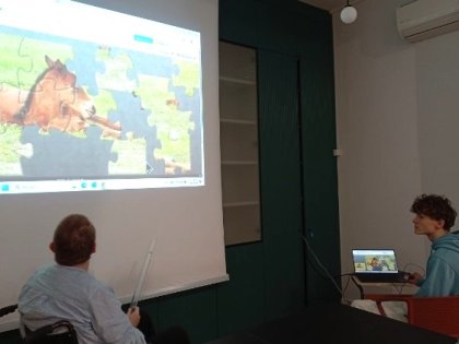 Na zdjęciu kobieta na wózku wpatrzona w duży kolorowy ekran