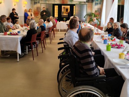 Widok sali na której przy długim stole siedzą starsze osoby spożywające posiłek świąteczny