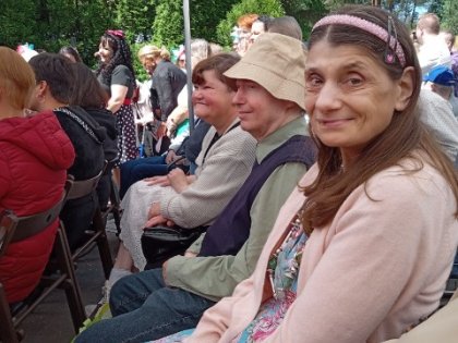 Na zdjęciu widać siedzącą uśmiechniętą kobietę obok niej mężczyzna w kapeluszu