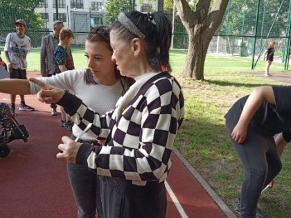 Na zdjęciu dwie kobiety rozmawiają ze soba wskazując palcamiw tle boisko szkolne