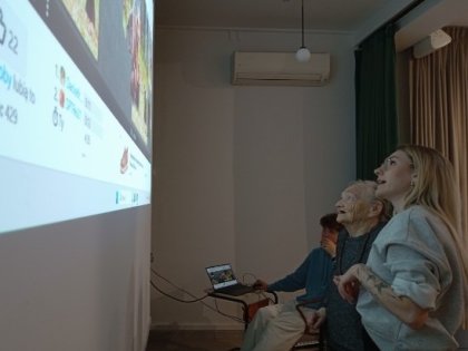 Na zdjęciu młoda kobieta ze starszą panią patrzą na kolorowy ekran.