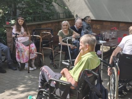 Na zdjęciu starsze osoby w radosnych pozach na tle ogrodu