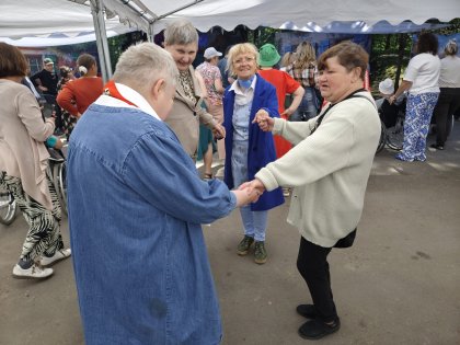Na zdjęciu trzy panie trzymając się za ręce tańczą wokół inne osoby trwa zabawa