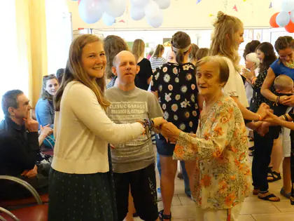 Wolontariuszka trzyma za ręce mieszkankę i mieszkańca podczas wspólnego tańca