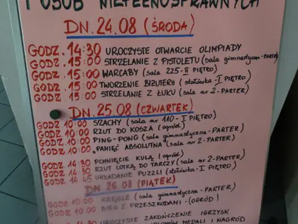 Tablica z programem Sportowej Olimpiady Seniorów i Osób Niepełnosprawnych w dniach 24–26 sierpnia: otwarcie, strzelanie, warcaby, szachy, ping-pong, kręgle, bieg z przeszkodami i bal olimpijczyka