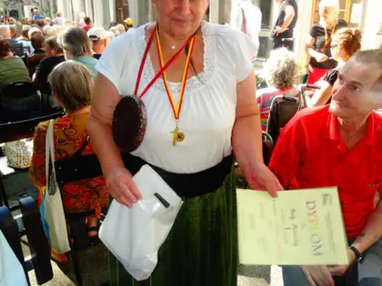Kobieta z medalami na szyi trzyma dyplom, w tle publiczność na dziedzińcu