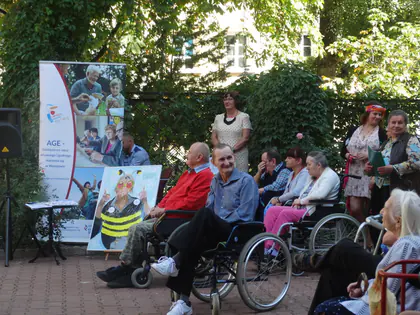 Mieszkańcy na wózkach przy stoisku z banerem projektu AGE podczas pikniku na podwórku