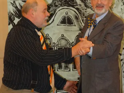 Dwóch aktorów kabaretu w kapeluszach tańczy przed dekoracją z rysunkiem kamienicy
