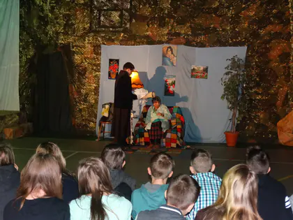Scenka misterium w pokoju z fotelem i lampą, młodzież siedzi na podłodze i ogląda