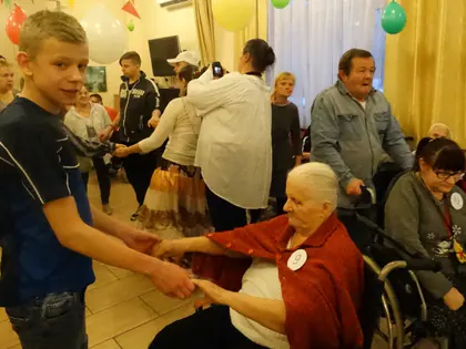 Chłopiec trzyma za ręce mieszkankę na wózku w czerwonym szalu podczas balu andrzejkowego