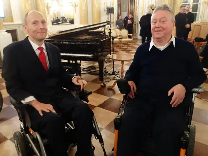 Dwaj mężczyźni na wózkach w eleganckiej sali z fortepianem podczas gali