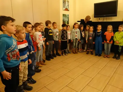 Rząd przedszkolaków stoi w świetlicy przed występem, w tle pianino i telewizor
