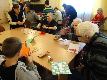 Chłopiec i starszy mieszkaniec wycinają ozdoby przy stole z kolorowymi kartkami