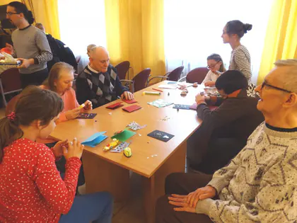 Dzieci i mieszkańcy siedzą przy stole i robią świąteczne ozdoby z papieru