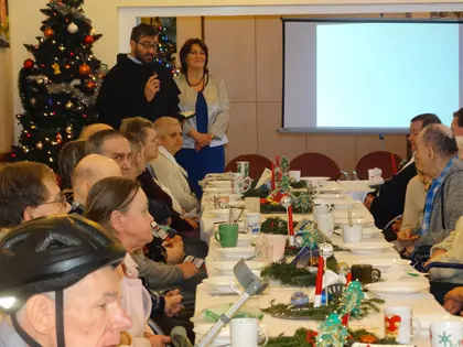 Zakonnik i kobieta przemawiają przy choince do mieszkańców siedzących przy stołach
