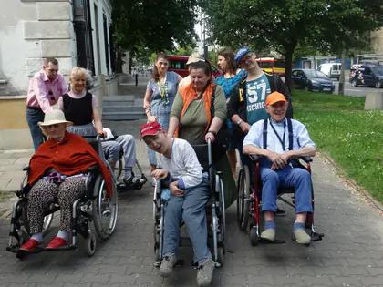 Opiekunowie pchają wózki z mieszkańcami chodnikiem w drodze do parku