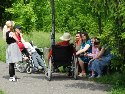 Mieszkańcy z opiekunami odpoczywają w cieniu drzew w Parku Traugutta