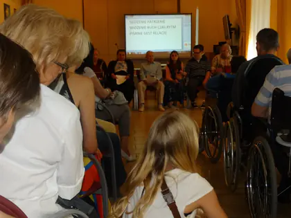 Widzowie, w tym osoby na wózkach, oglądają spektakl, na ekranie wyświetlany tekst
