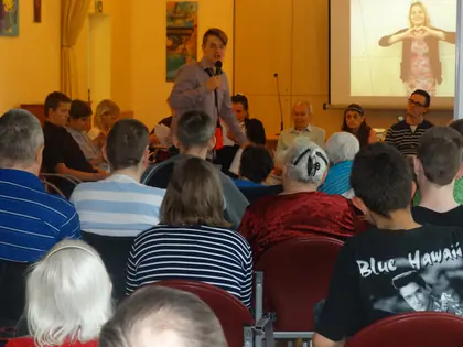 Chłopiec mówi do mikrofonu wśród widzów, na ekranie młoda kobieta z gestem serca