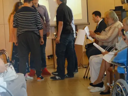 Młodzi aktorzy przechodzą między mieszkańcami siedzącymi na wózkach