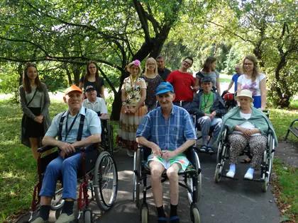 Mieszkańcy na wózkach i wolontariusze pozują na alejce w parku