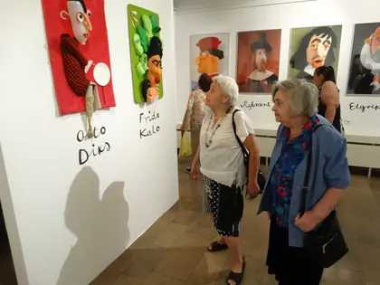 Mieszkanki oglądają w muzeum karykatury kolorowe portrety znanych malarzy