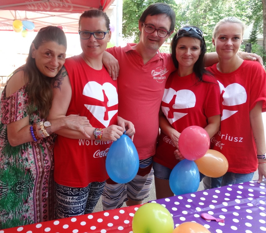 Wolontariusze w czerwonych koszulkach z sercem i mieszkańcy trzymają balony.