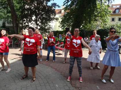 Wolontariusze w czerwonych koszulkach prowadzą wspólną gimnastykę na podwórku