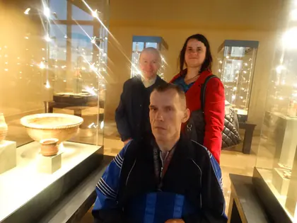 Trzech uczestników wycieczki pozuje w muzeum przy gablocie z misą