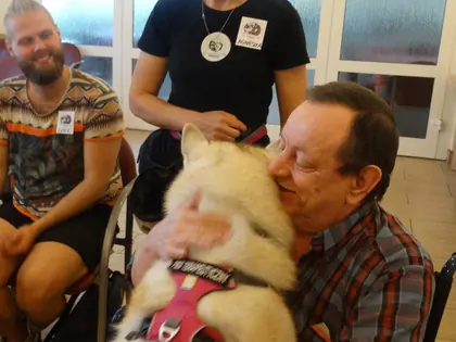 Starszy mężczyzna na wózku obejmuje psa husky w różowych szelkach