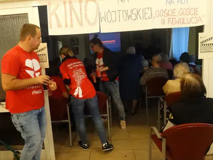Wolontariusze w czerwonych koszulkach w świetlicy z napisem Kino na Wójtowskiej, zapraszamy na film