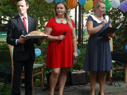 Mężczyzna z tacą chleba i dwie prowadzące z mikrofonami podczas festynu w ogrodzie
