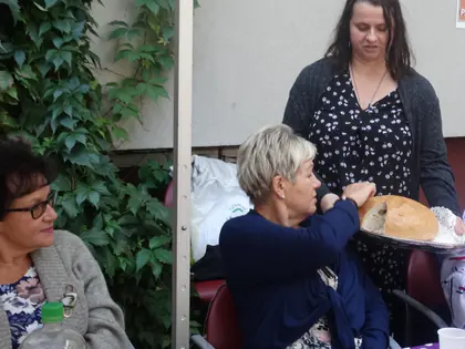 Mieszkanki przy stole w ogrodzie, kobieta podaje tacę z chlebem