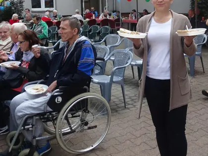 Kobieta w białej bluzce roznosi talerzyki z poczęstunkiem między mieszkańcami na podwórku