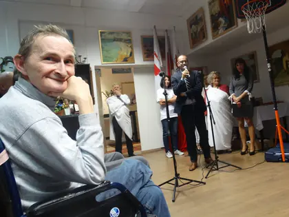 Uśmiechnięty mieszkaniec na wózku, w tle prowadzący z mikrofonem i flagi podczas zawodów