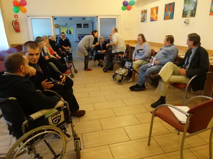 Mieszkańcy i goście siedzą w kręgu w świetlicy podczas spotkania