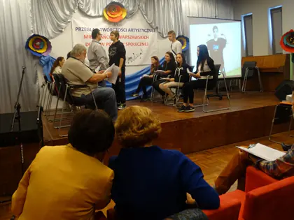 Występ na scenie przeglądu, widzowie siedzą przed sceną, w tle ekran z projekcją