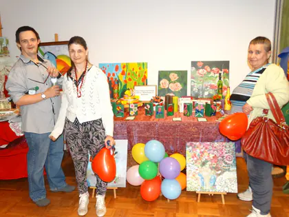 Mieszkańcy pozują przy stoisku z obrazami i balonami na przeglądzie twórczości