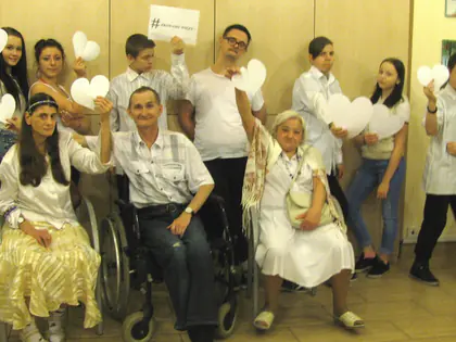Uczestnicy spektaklu w bieli, część na wózkach, trzymają papierowe serca i kartki