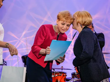 Dwie kobiety rozmawiają na scenie, jedna trzyma niebieski dyplom
