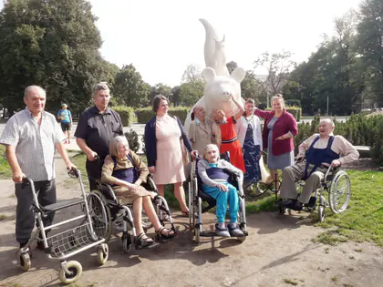 Mieszkańcy z opiekunkami przy rzeźbie w Parku Fontann
