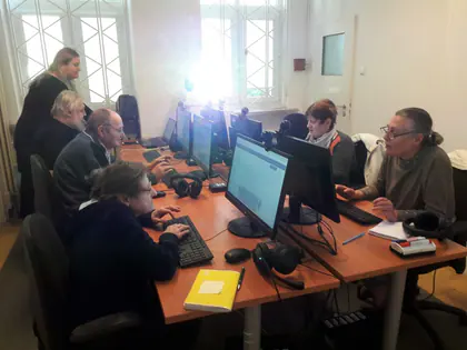 Seniorzy pracują przy komputerach, prowadząca pomaga jednej z uczestniczek