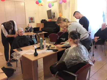 Kilka fryzjerek czesze mieszkanki w świetlicy przy stołach z akcesoriami