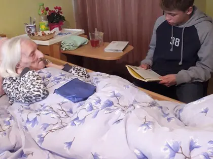 Nastolatek czyta książkę starszej mieszkance leżącej w łóżku