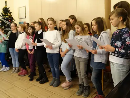 Dziewczęta śpiewają kolędy z kartek przy choince