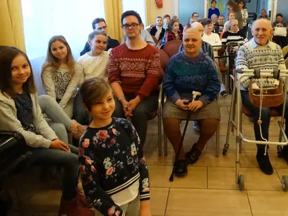 Uczennice i mieszkańcy siedzą razem w świetlicy podczas kolędowania