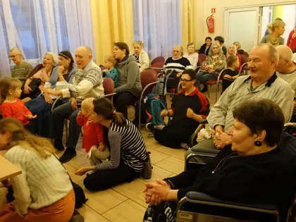 Dzieci siedzą na podłodze przed mieszkańcami podczas kolędowania